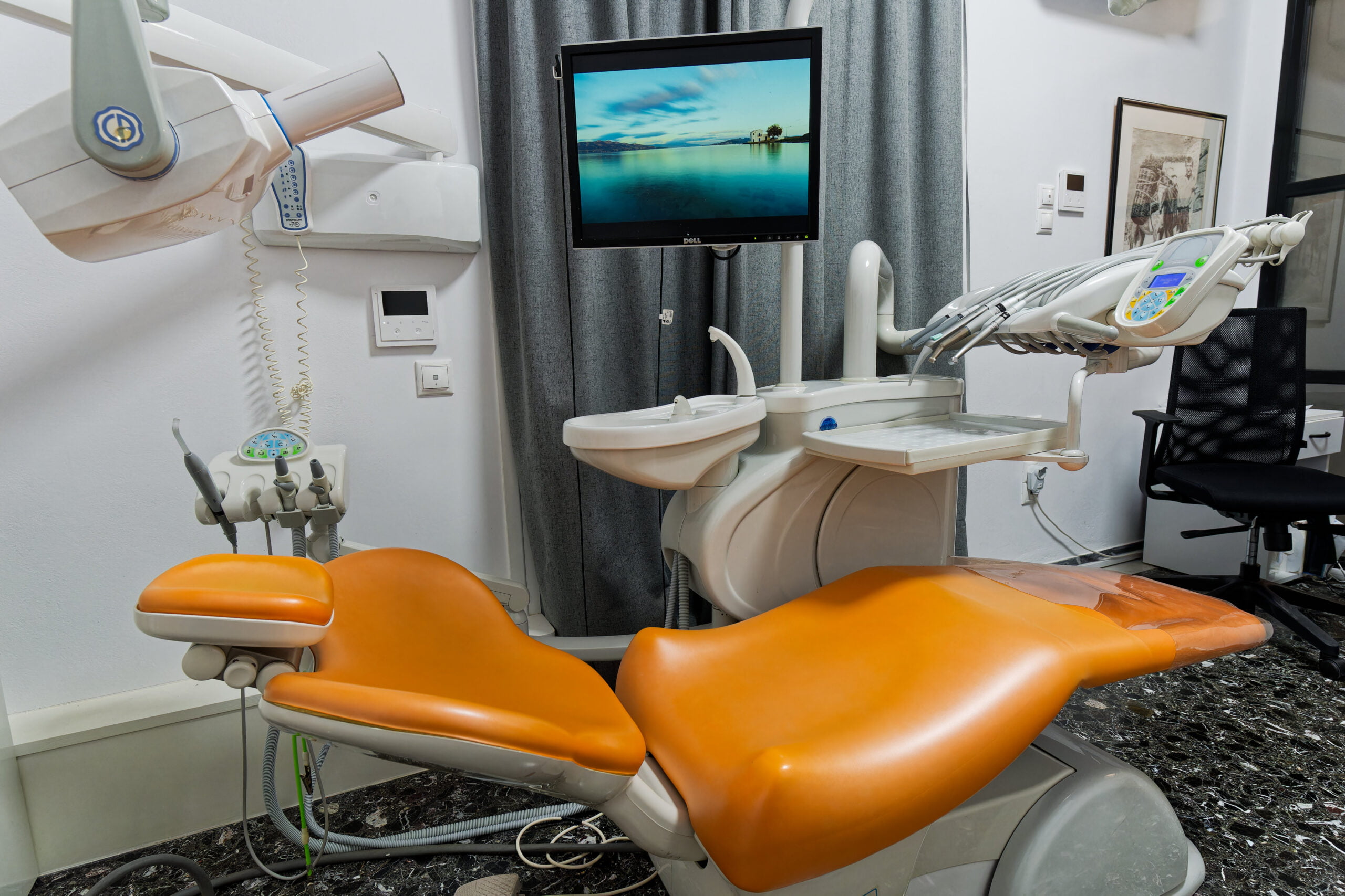 Dental operatory with orange chair, monitor, and equipment at Salamina Clinic.