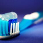 Blue toothbrush with soft bristles and toothpaste on blue background