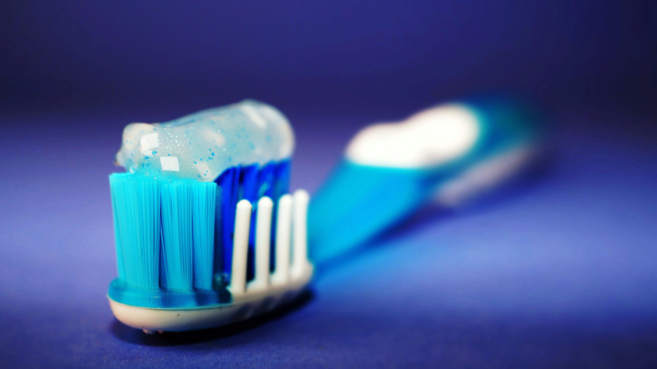 Blue toothbrush with soft bristles and toothpaste on blue background